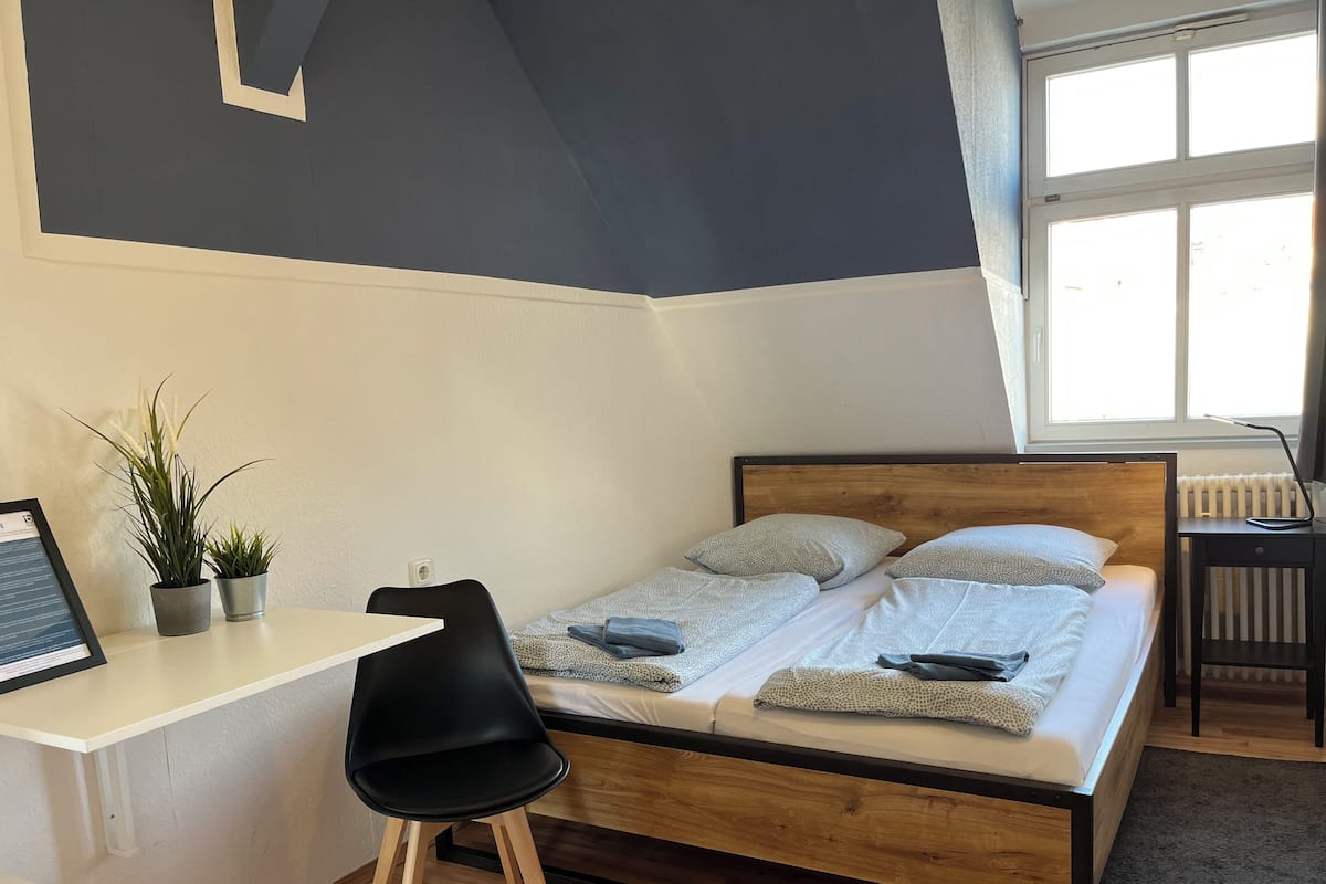 A bedroom with a bed, a desk, a chair, and two potted plants.