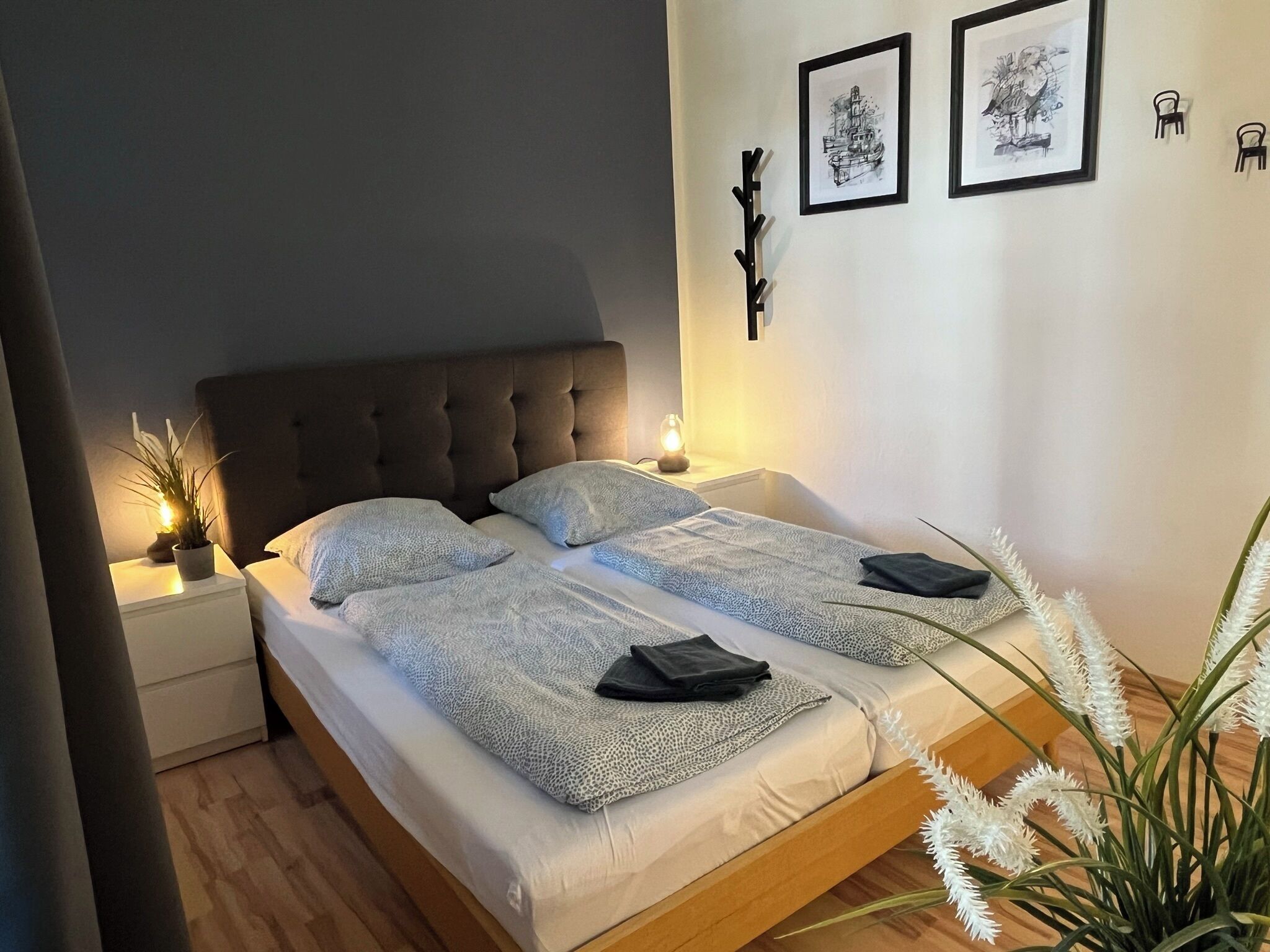 A neatly made bed with a tufted headboard, two bedside tables with lamps, and framed artwork on the wall.