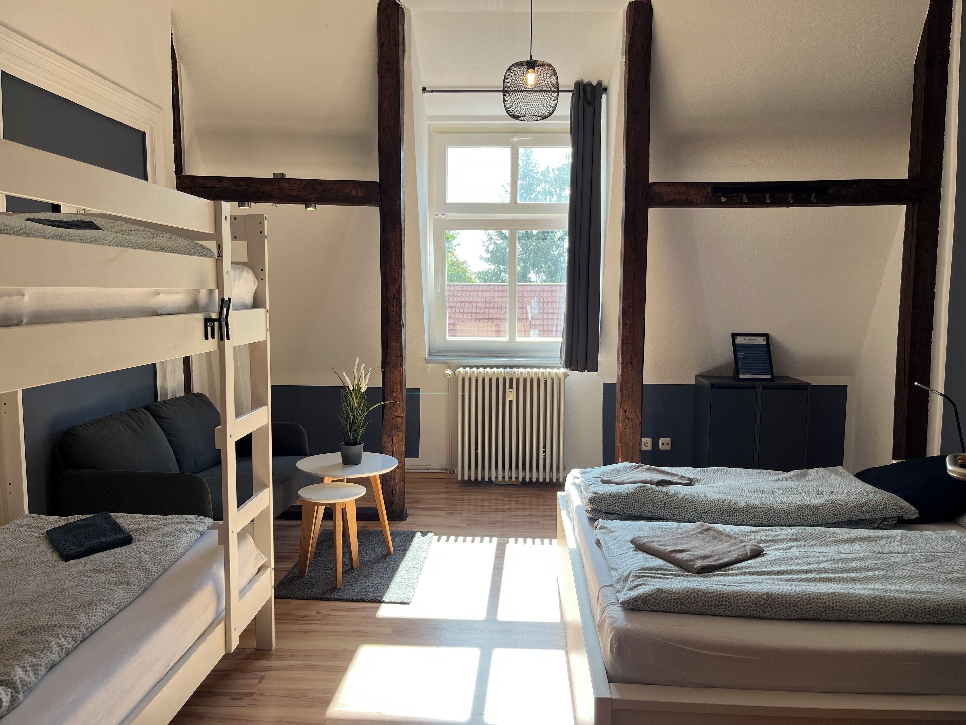 Habitación tipo dormitorio con literas, una pequeña mesa redonda con una planta, un radiador y una ventana con cortinas.