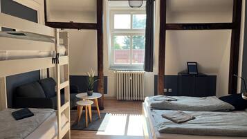 Habitación tipo dormitorio con literas, una pequeña mesa redonda con una planta, un radiador y una ventana con cortinas.
