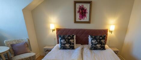 A hotel room with a large bed, two nightstands, a chair, and a framed artwork on the wall.