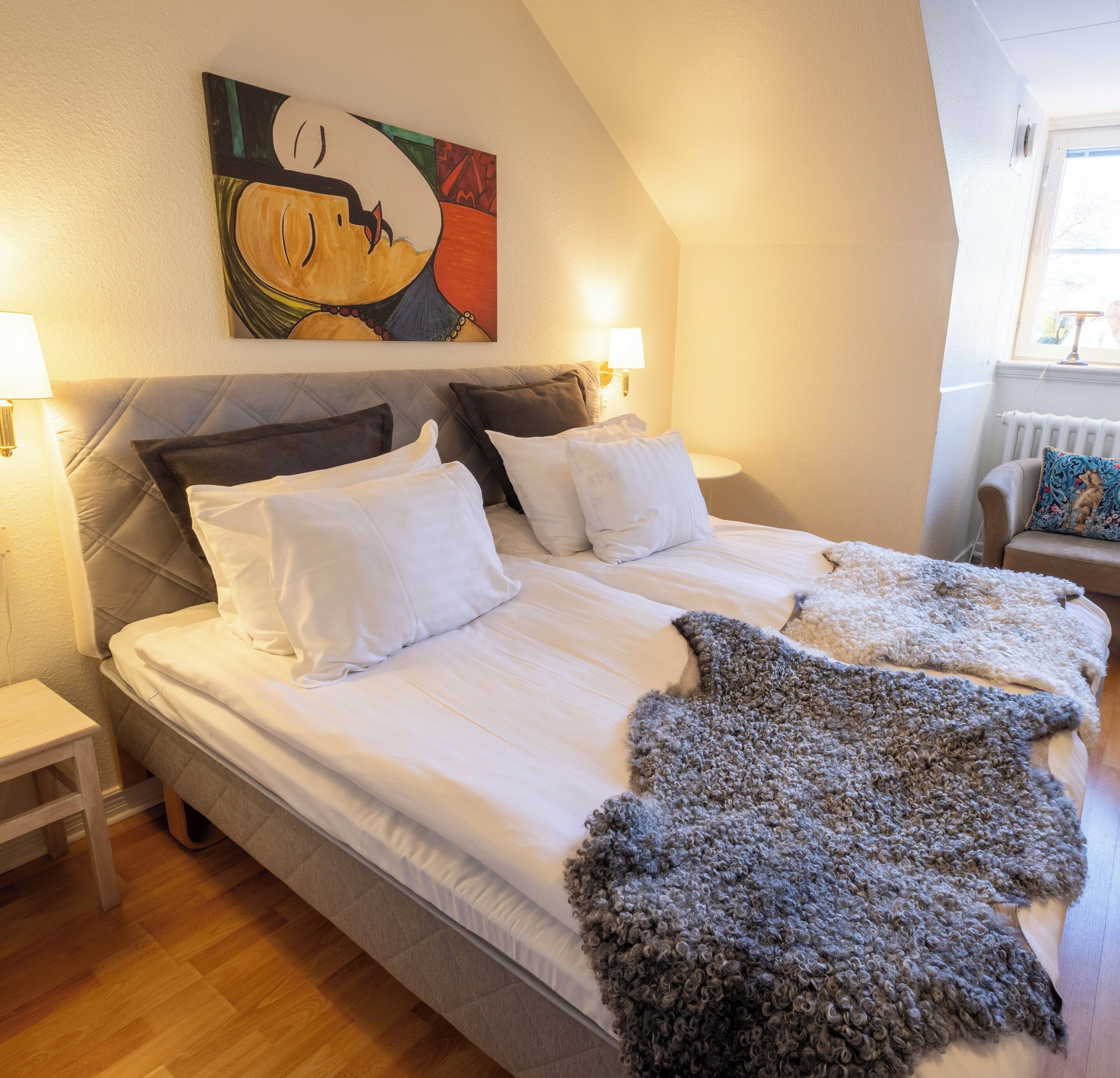 A double bed with white linens, a gray headboard, and a colorful abstract painting above it.
