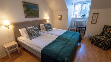 A bedroom with a bed, two bedside lamps, a small table, a chair, and a window with a view of the outside.