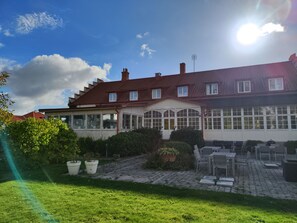 A two-story building with a red-tiled roof, large windows, and a patio area with outdoor furniture. - Anita på Gästis i Anderslöv (Trelleborg)