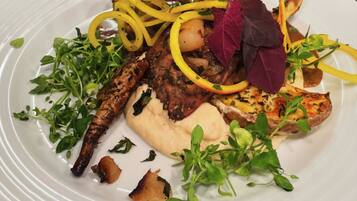 Um prato branco com diversos alimentos, incluindo carne grelhada, legumes e um molho cremoso.