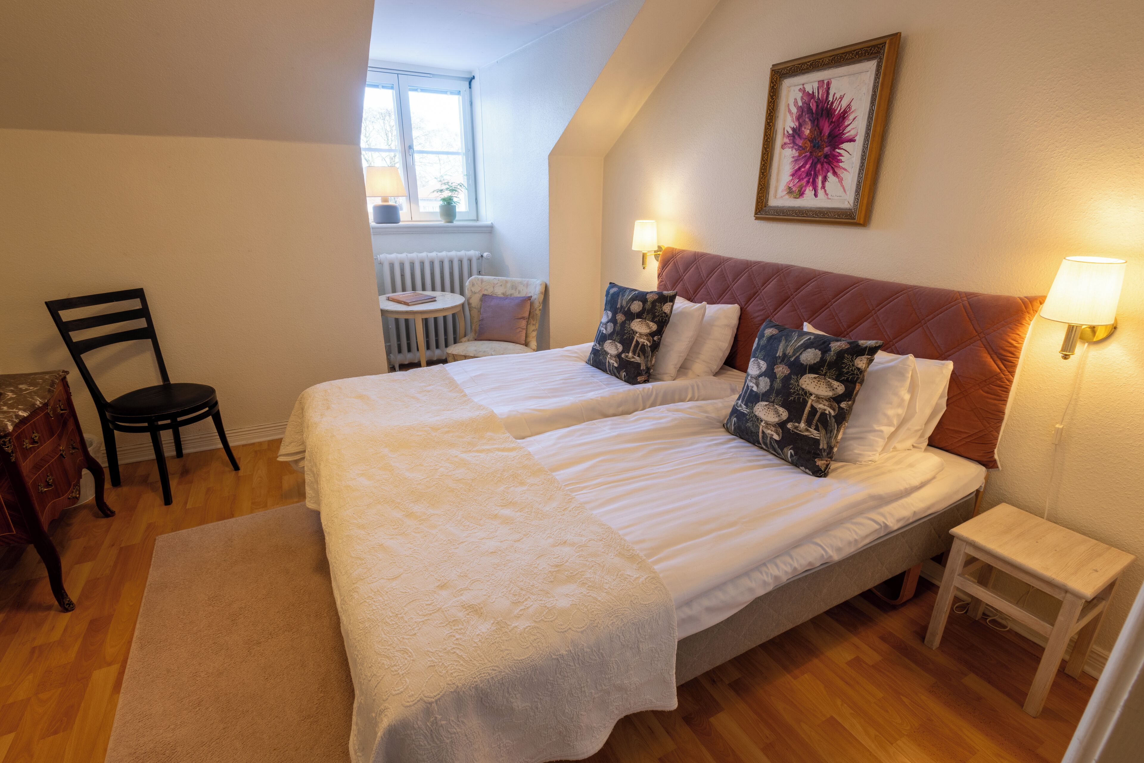 A bedroom with two beds, a small table, a chair, and a radiator.