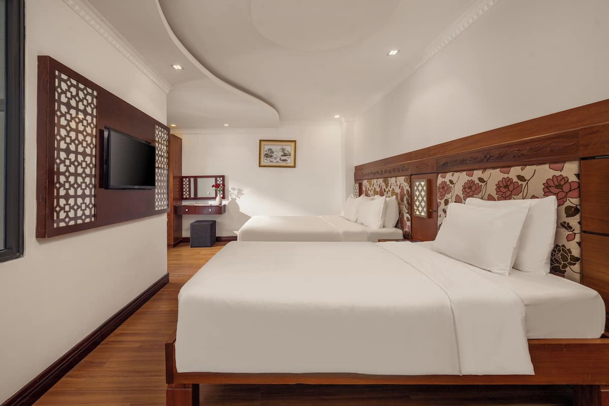 Une chambre d’hôtel avec deux lits, une télévision, un paravent décoratif et une œuvre d’art encadrée au mur.