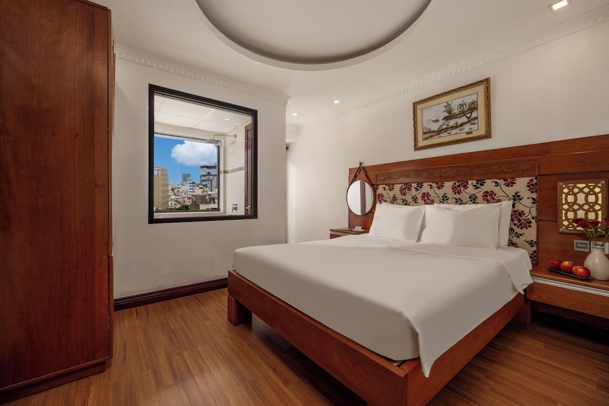 Une chambre d’hôtel avec un grand lit, une tête de lit en bois, une table de chevet, un miroir et une fenêtre donnant sur la ville.