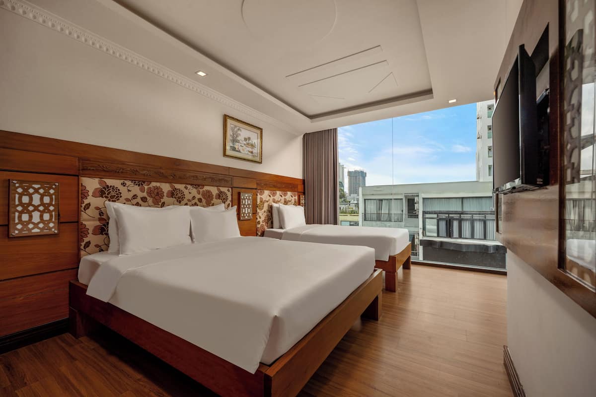 Une chambre d’hôtel avec un grand lit, deux tables de chevet, une tête de lit en bois, un tableau encadré, une grande fenêtre et une vue sur la ville.