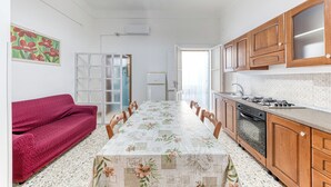 A kitchen with wooden cabinets, a dining table with chairs, a red sofa, and a refrigerator.