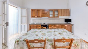 A compact kitchen with wooden cabinets, a dining table with a floral tablecloth, and a television above the counter.