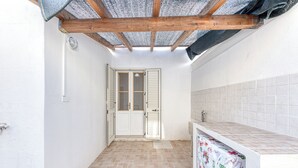 A narrow, tiled kitchen with a wooden ceiling, a white sink, and a door with shutters.