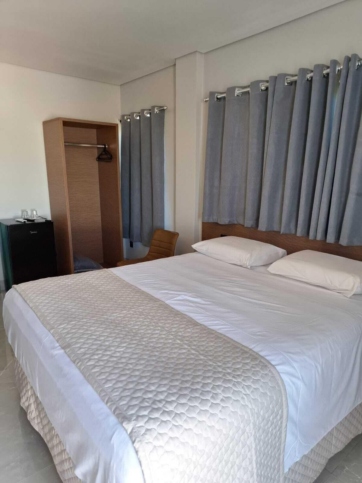 A hotel room with a large bed, a wooden wardrobe, and grey curtains.