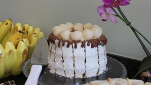 A cake with white frosting and chocolate drizzle, surrounded by bananas and an orchid.