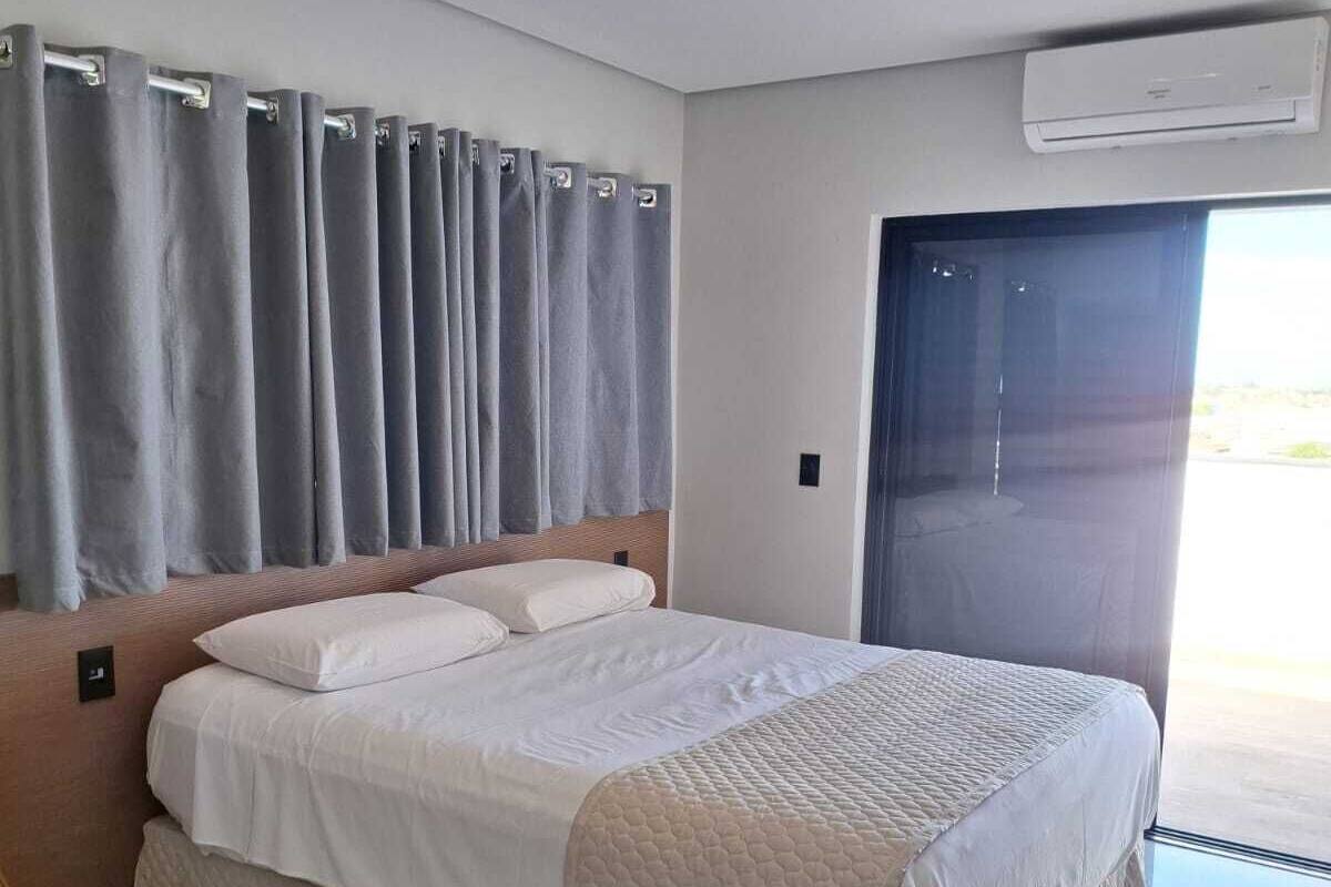 Een moderne slaapkamer met een groot bed, grijze gordijnen, een airconditioning en uitzicht door een deur.