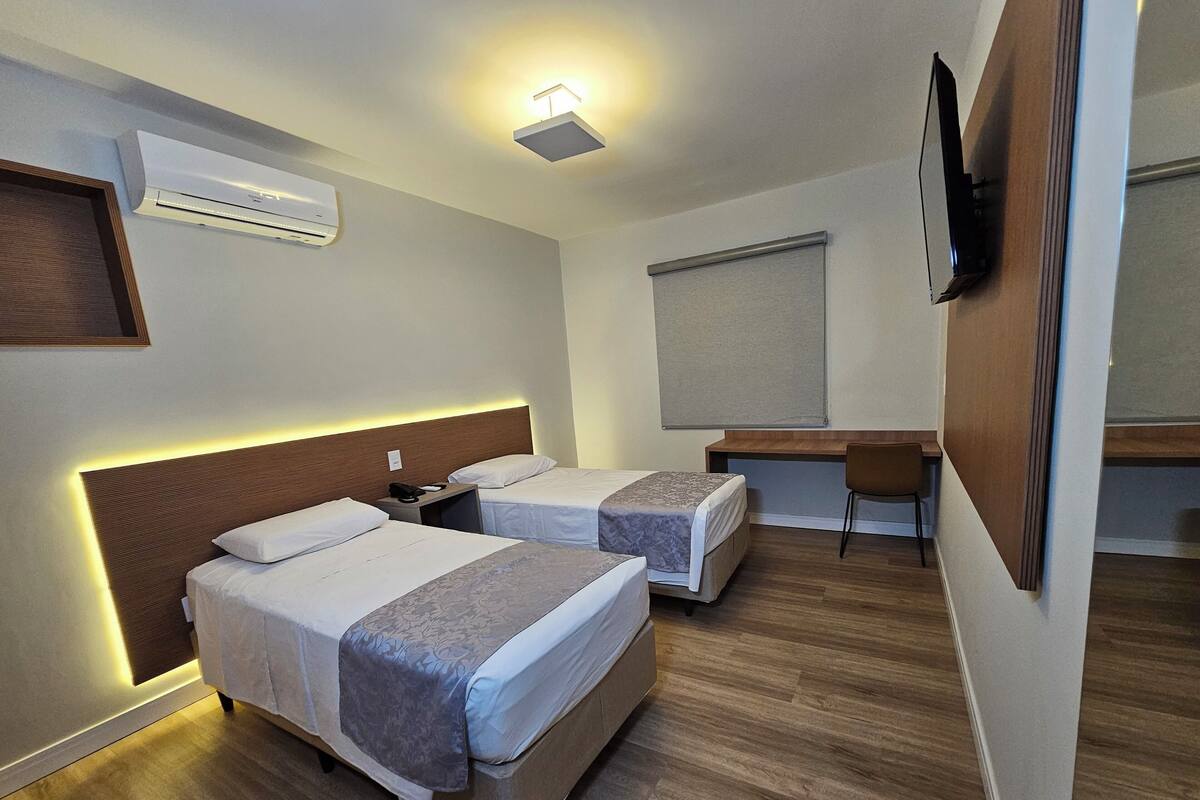 Een hotelkamer met twee bedden, een bureau, een stoel, een flatscreen televisie, een airconditioner en een plafondlamp.