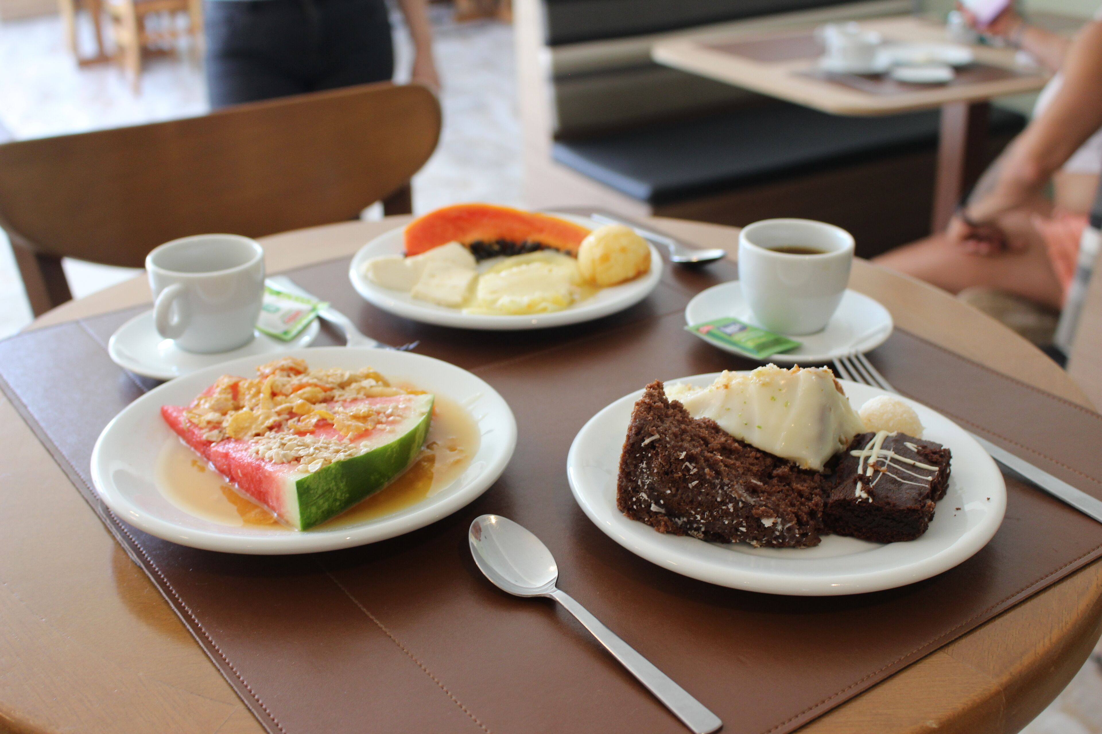 Uma mesa de jantar com pratos de comida, incluindo uma fatia de melancia, um pedaço de bolo e uma xícara de café.