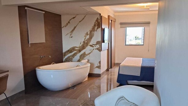 A modern bathroom with a freestanding bathtub, a marble wall, and a white armchair.