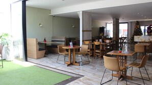 A modern indoor dining area with wooden tables and chairs, a green artificial turf area, and a large window providing natural light.