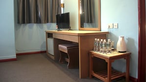 A hotel room with a desk, a television, a mirror, a bench, and a small table with bottles and a vase. - Hotel O Hotel Ramai (Sandakan)