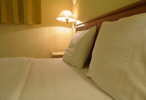 Cama bem arrumada com lençóis e almofadas brancas, uma mesa de cabeceira e um abajur.