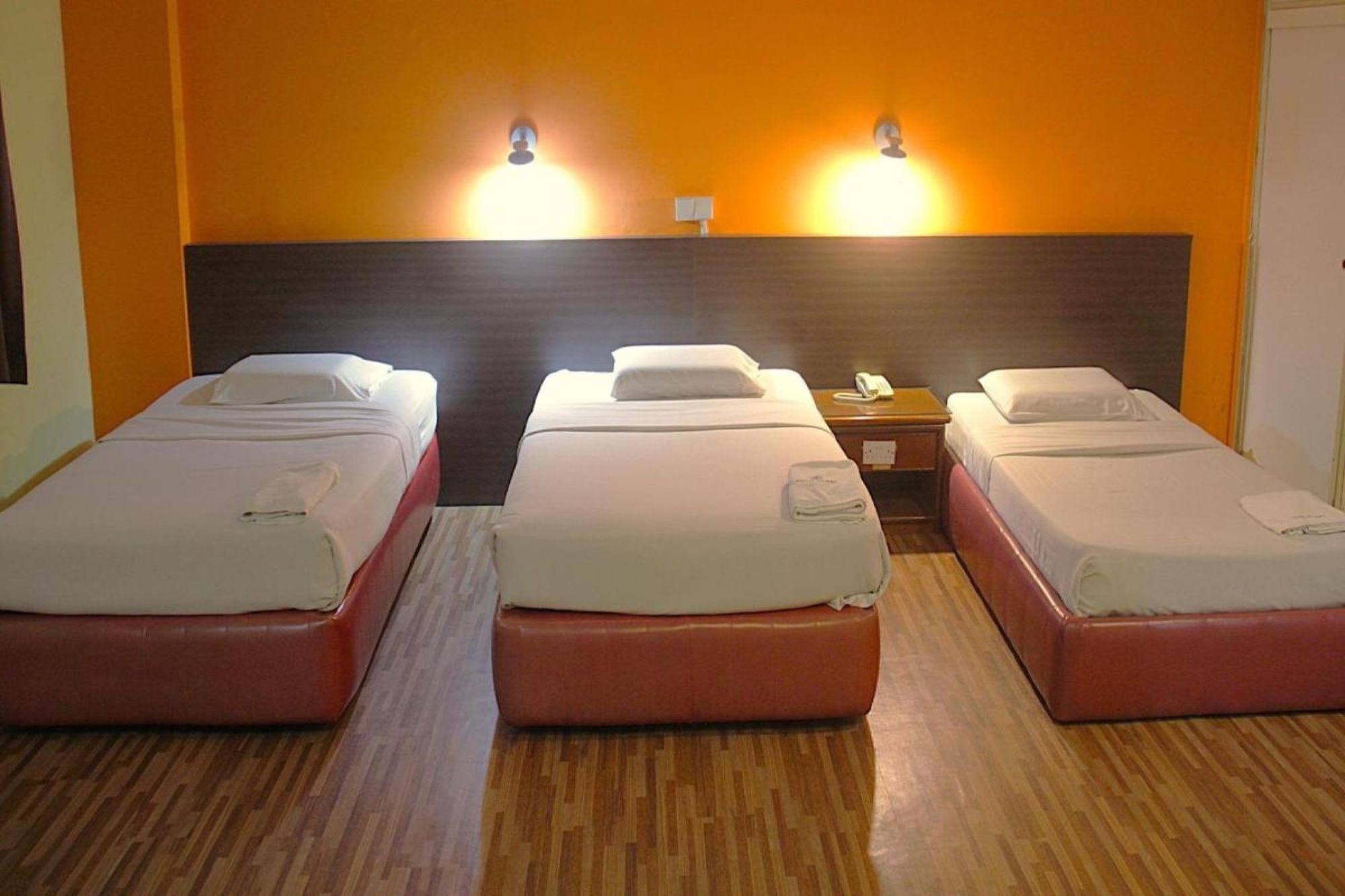A hotel room with two single beds, a wooden floor, and two wall-mounted lights.