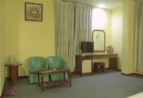 Una habitación con un sofá verde, una pequeña mesa de madera, un televisor y un escritorio con un espejo.