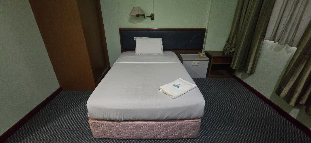 Una habitación de hotel con una cama, una mesita de noche, una lámpara y un ventanal con cortinas.