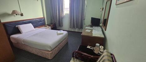 A hotel room with a bed, a desk, a chair, a mirror, a lamp, and curtains.