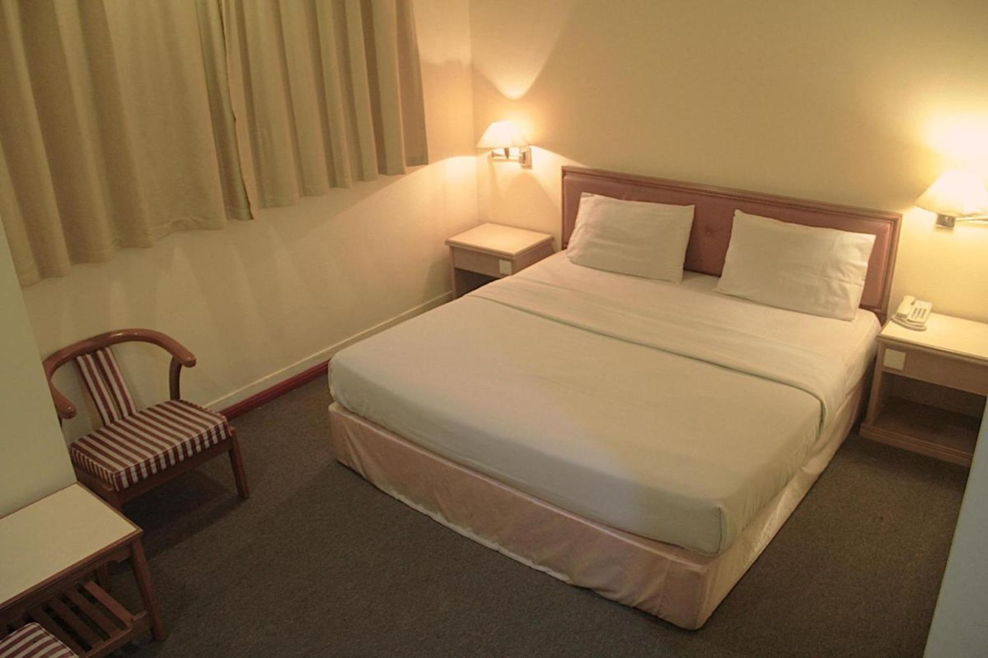 Una habitación de hotel con una cama individual, mesitas de noche, una silla y una lámpara.