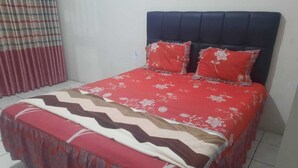 A bed with a red floral bedspread and two pillows, a striped blanket, and a curtain. - Hotel O Home Stay Syariah Annur (Jalaksana)