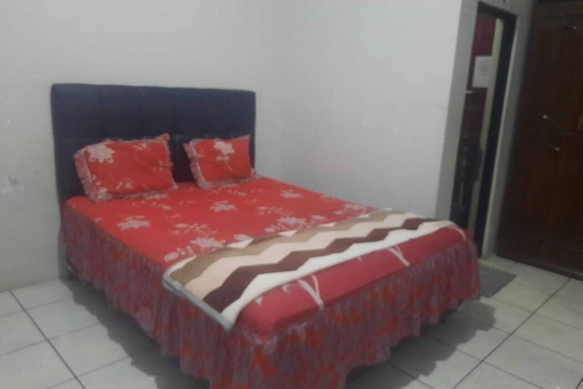 A bed with a red and white patterned bedspread and matching pillows, a dark headboard, and a tiled floor.