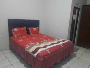 A bed with a red and white patterned bedspread and matching pillows, a dark headboard, and a tiled floor. - Hotel O Home Stay Syariah Annur (Jalaksana)