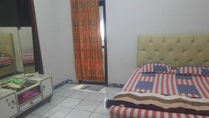 A bedroom with a bed featuring an American flag design, a bedside table with a mirror, and a wardrobe with a patterned curtain. - Hotel O Home Stay Syariah Annur (Jalaksana)