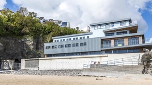 A modern building with multiple floors, large windows, and a stone wall on one side. - Harbour Stays - The Marine Centre (Saundersfoot)