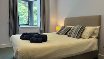 A neatly made bed with striped pillows and rolled towels, a bedside lamp, and a window with curtains.