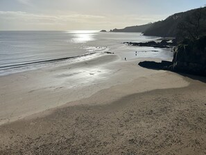 A beach with a clear view of the sea, rocky cliffs, and a few people walking. - Harbour Stays - The Marine Centre (Saundersfoot)