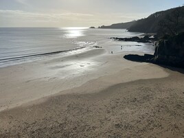 A beach with a clear view of the sea, rocky cliffs, and a few people walking.