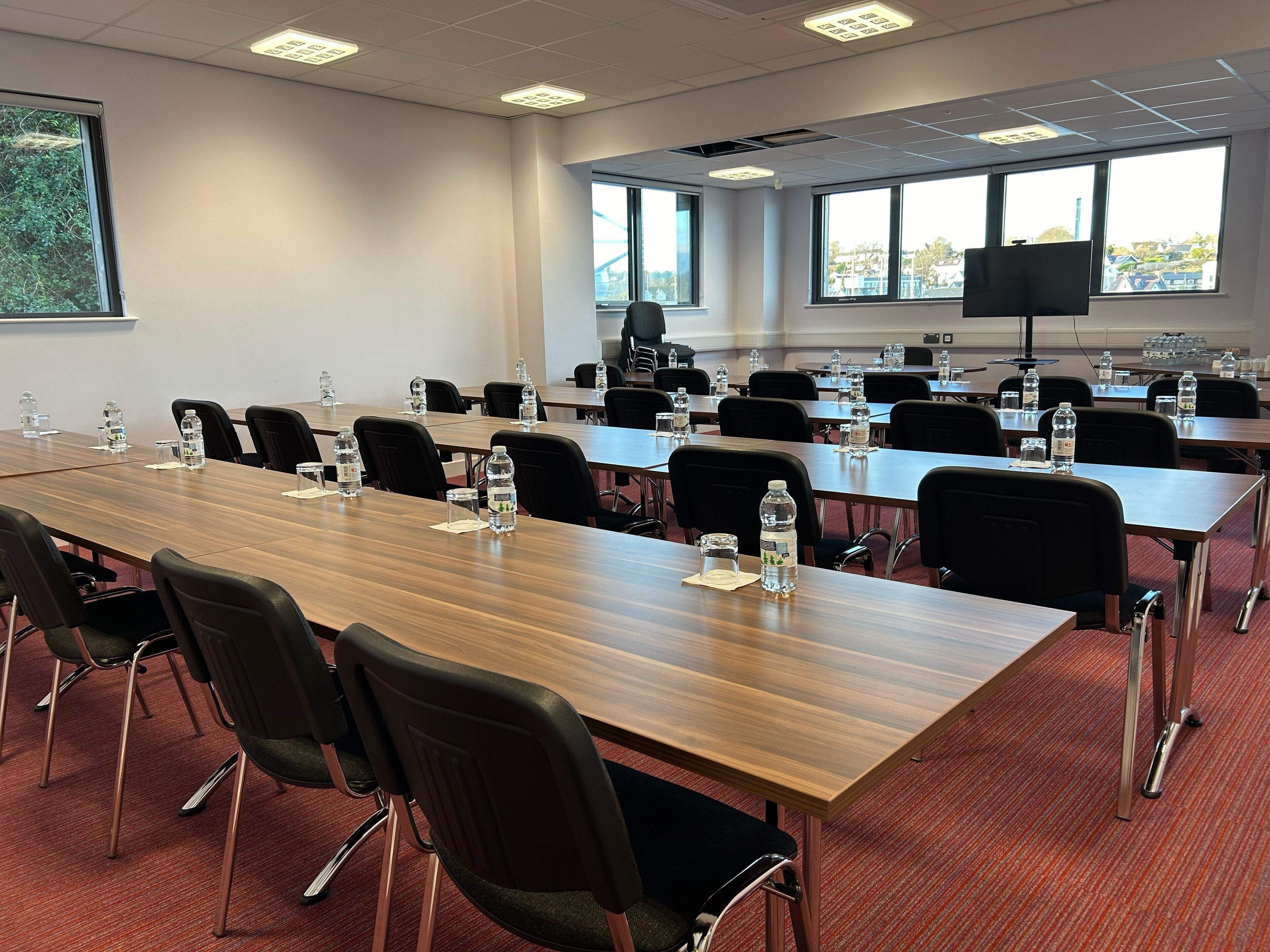 A conference room with long tables, chairs, water bottles, and a large screen.