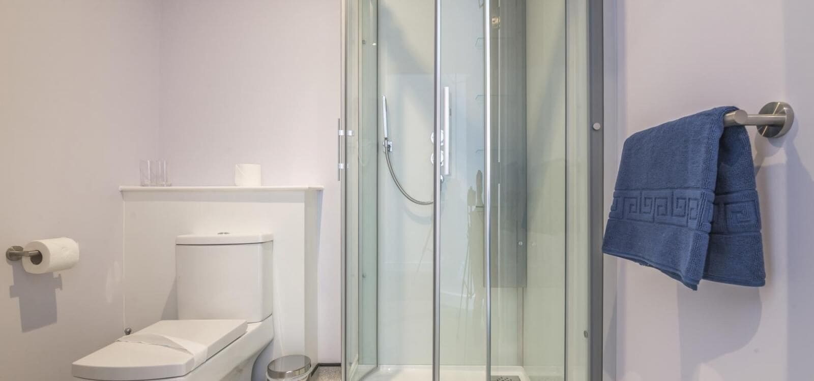 Ein modernes Badezimmer mit einer Glaskabine zur Dusche, einer Toilette und einem Handtuchhalter mit einem blauen Handtuch.
