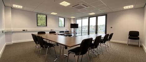 Une salle de conférence avec une longue table, des chaises, un téléviseur et de grandes fenêtres donnant sur un beau paysage.