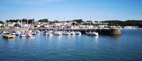 Un puerto con numerosos barcos amarrados, un muelle de piedra y edificios residenciales al fondo.