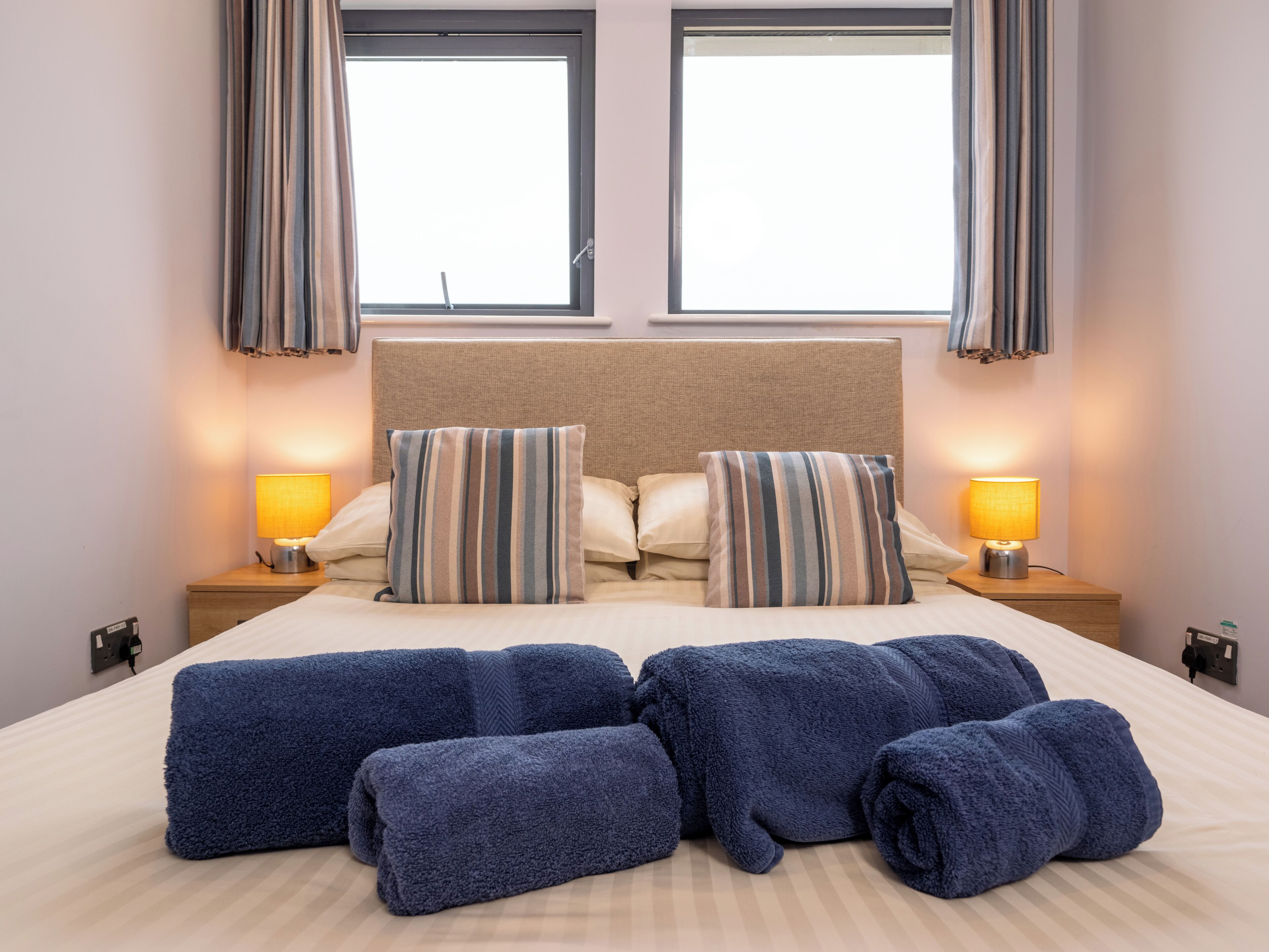 Une chambre d’hôtel avec un lit, deux oreillers, deux lampes de chevet et une fenêtre avec des rideaux.