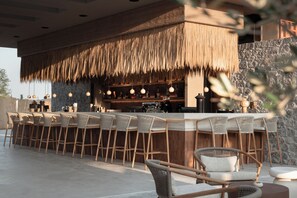 Zona de bar al aire libre con techo de paja, taburetes y lámparas colgantes.