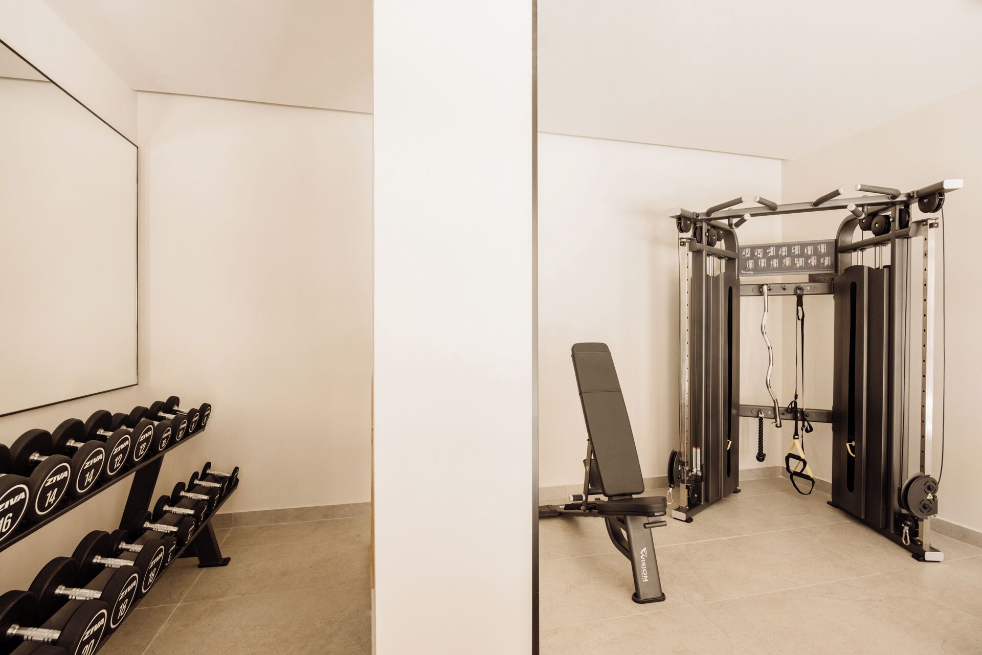 Un gimnasio con barra de pesas, mancuernas y máquina de poleas.
