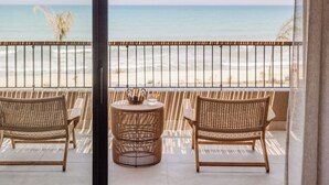 A balcony with two wicker chairs, a small round table, and a view of the beach and ocean.