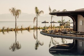 A serene pool area with lounge chairs and umbrellas, surrounded by palm trees and a view of the sea. - Unda (Corfu)