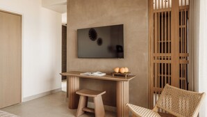 A modern room with a wooden desk, a television mounted on the wall, a wicker chair, and a wooden door.