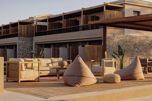 A modern outdoor seating area with wicker furniture and geometric cushions, set against a stone wall and wooden pergola.