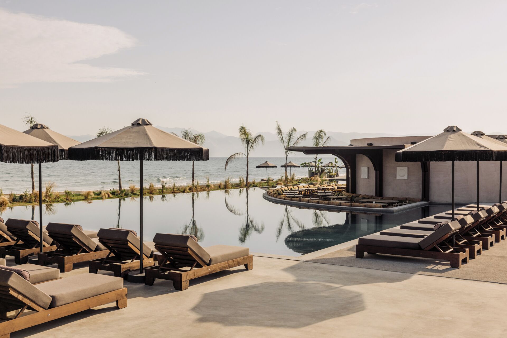 A poolside area with lounge chairs and umbrellas, a small pool, and a view of the sea.